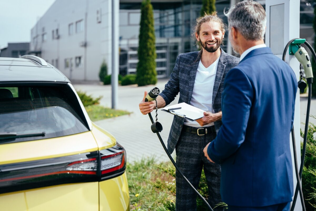 Two,men,near,car,charging,station.,young,confident,salesman,showing