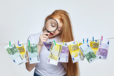 Beautiful,red Haired,girl,examines,euro,banknotes,through,a,magnifying,glass.