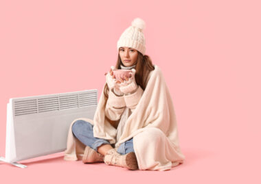Frozen,young,woman,with,cup,of,hot,cocoa,near,radiator