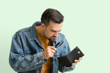 Angry,young,man,with,magnifier,and,empty,wallet,on,green