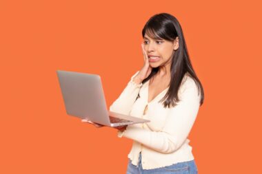 Concerned,woman,reacts,while,using,laptop,against,bright,orange,background