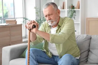 Senior,man,with,stick,suffering,from,parkinson,syndrome,on,sofa