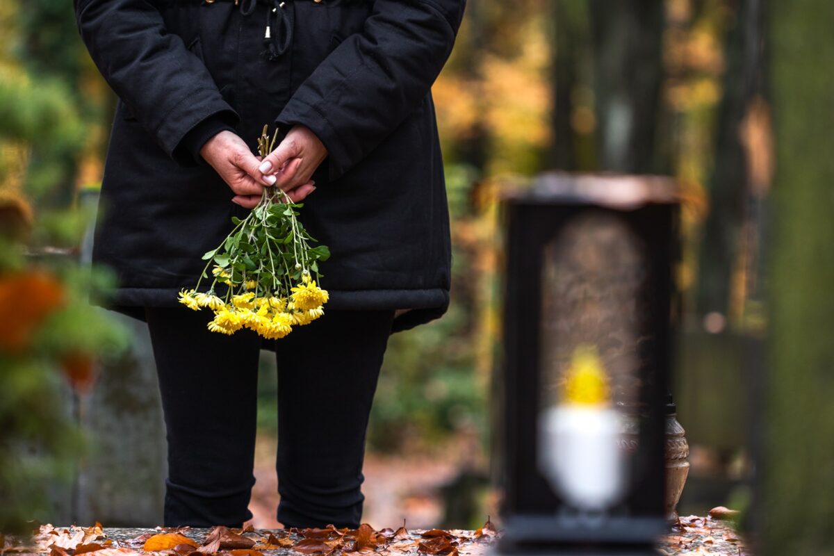 Mourning,woman,holding,flowers,in,hands,and,standing,at,grave
