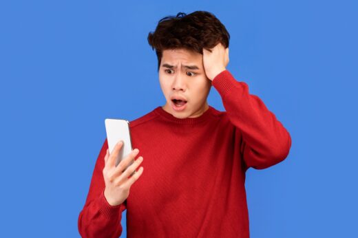 Surprised,shocked,asian,man,using,mobile,phone,on,blue,wall