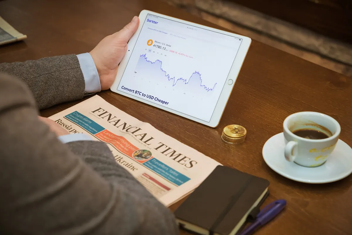 Tablette affichant un graphique de prix, journal financier, tasse de café et accessoires de bureau.