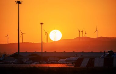 Coucher de soleil orange vif, éoliennes silhouettées, aéroport avec avions.