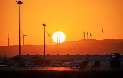 Coucher de soleil orange vif, éoliennes silhouettées, aéroport avec avions.