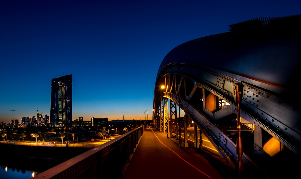 Paysage urbain nocturne avec pont illuminé et gratte-ciel à l'horizon.