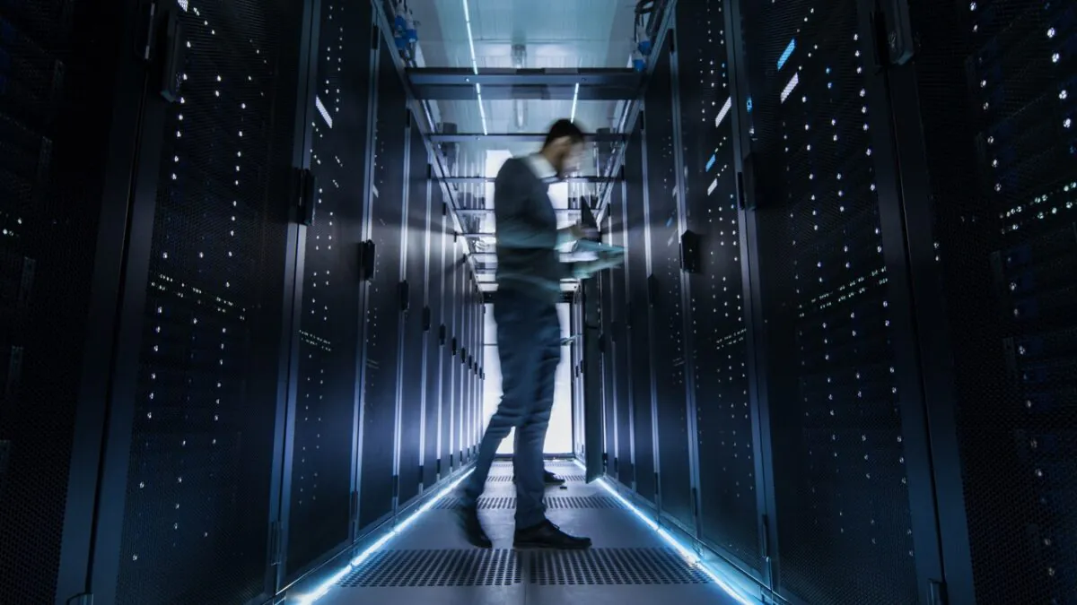Male,it,engineer,walking,and,working,in,data,center,corridor.