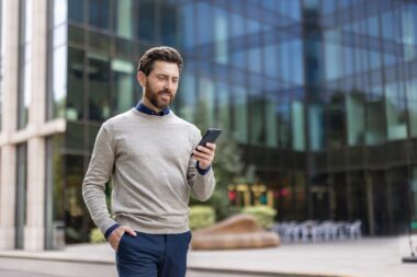 Smiling,young,man,walking,near,office,center,and,using,mobile